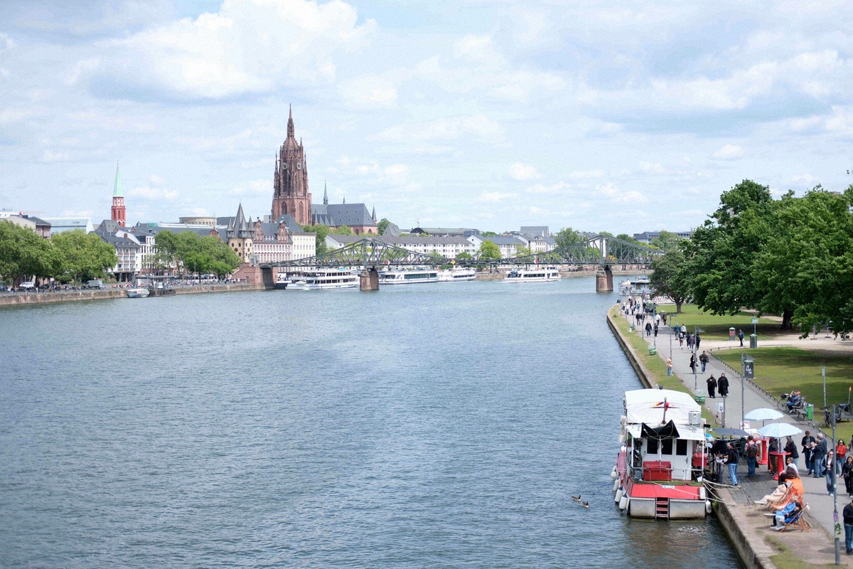 Weites Panorama des Mainufers mit Ausflugsbooten, dem Eisernen Steg und dem Turm des Kaiserdoms im Hintergrund